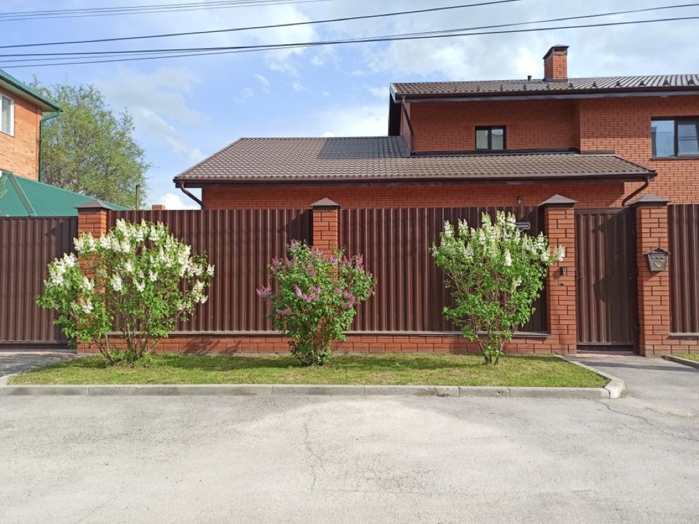 Maison en briques avec une clôture à panneaux métalliques et des lilas en fleurs